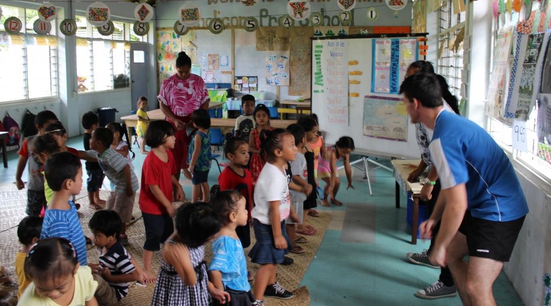 Two volunteers encourage children to exercise with a fun physical activity during class in Samoa. Projects Abroad volunteers teach a fun physical game to children to get them active and moving in Samoa.